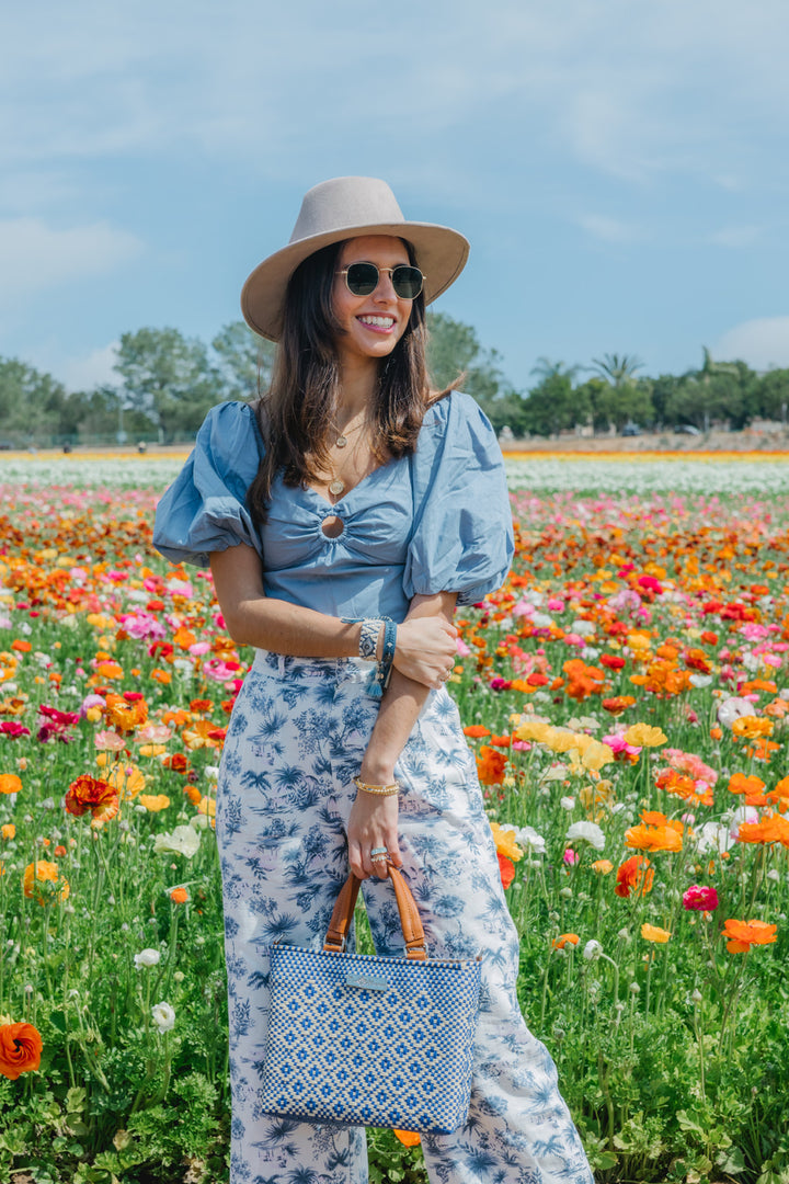 Woman wearing Mixte woven crossbody drawstring bag — blue and beige medium bag with tan leather crossbody handmade from recycled plastic, Tin Marin