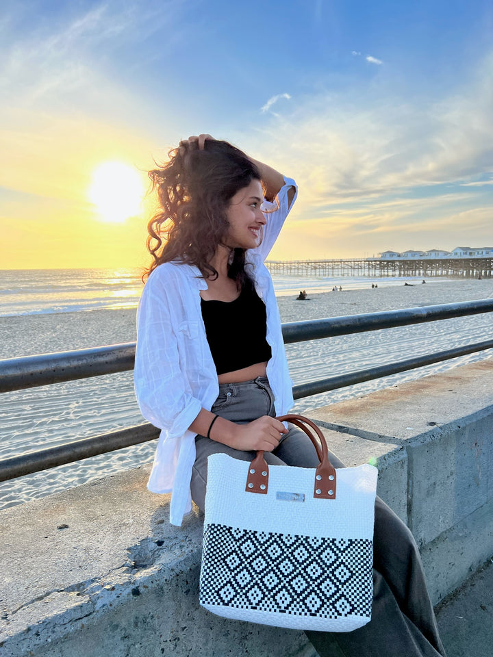 Woman wearing Tin Marin White Large woven crossbody bag in white and black with tan leather— handmade from recycled plastic in Mexico by Tin Marin